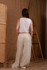 Back view of beige women's linen trousers with a white muslin top. The lightweight linen fabric ensures coolness and style, reflecting effortless elegance for warm climates like the GCC region. Ideal for casual strolls and beach getaways.
