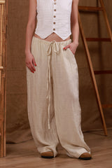 Beige women's linen trousers styled with a white bikini top and a long white linen kimono. This resort-ready outfit is perfect for beach days, reflecting a minimalist yet sophisticated style. The natural linen fabric ensures breathability and comfort in the hot GCC climate.