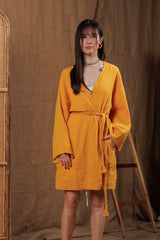 Front view of a yellow muslin robe with a wrap-around belt, perfect for layering over summer outfits in Dubai and GCC. Designed from breathable muslin fabric, it provides comfort and style for beach and city wear. Captured in a natural, minimalist interior, reflecting sustainable Middle Eastern fashion.