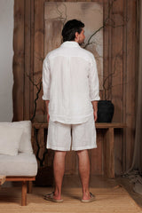 Back view of a white linen shirt paired with relaxed-fit linen drawstring shorts, designed for the hot climates of Dubai, UAE, and GCC. The minimalist, natural-themed setting with wooden accents reflects sustainable Middle Eastern fashion. Ideal for beach, city, and home wear during summer.