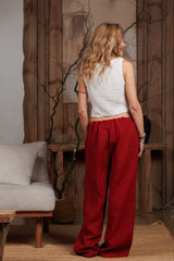 Back view of women's burgundy linen trousers showcasing the loose fit and lightweight texture. Paired with a white sleeveless top for a chic and effortless look. Perfect for warm weather and modern minimalist wardrobes in the UAE and GCC.