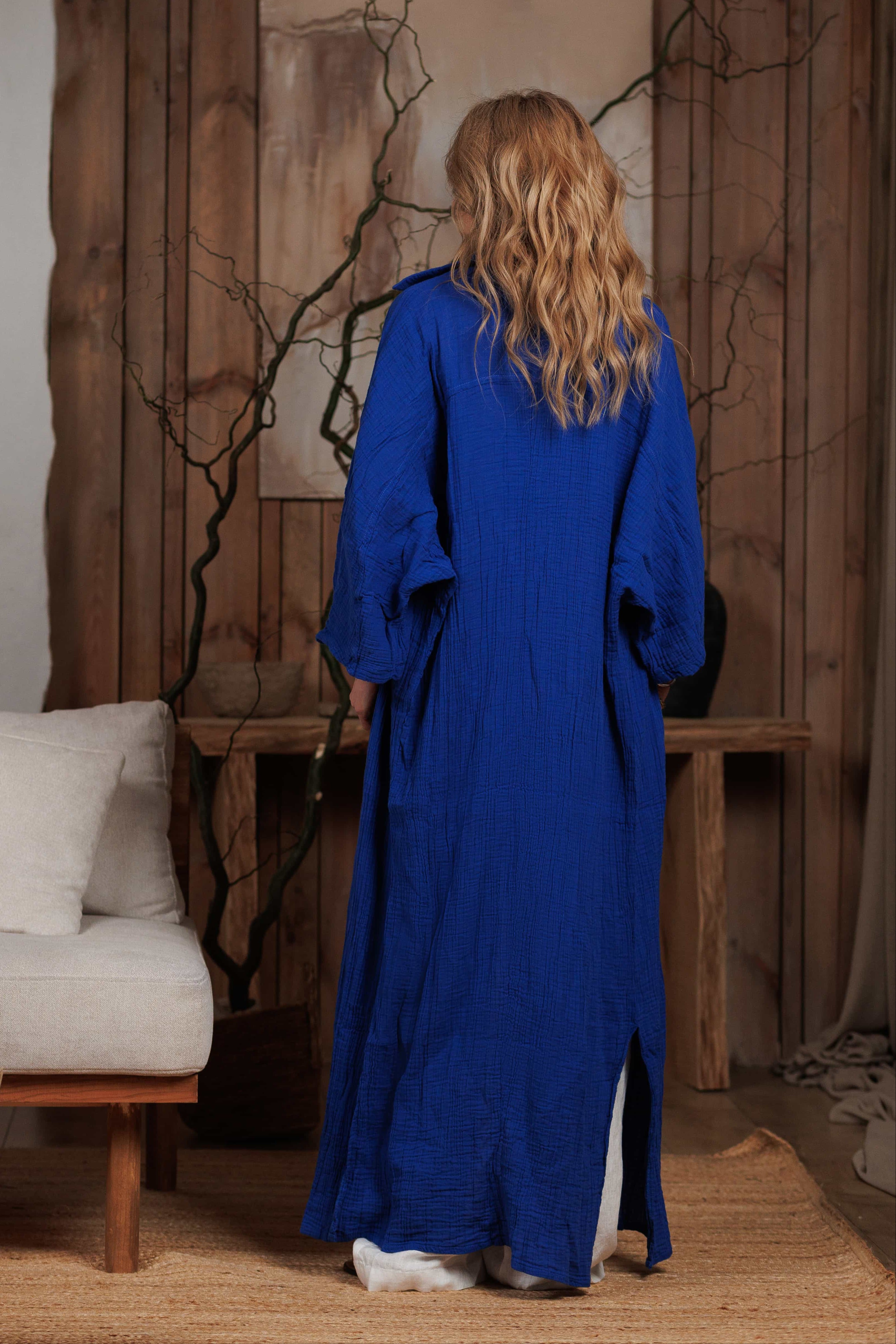 Back view of a long electric blue muslin shirt with a flowy silhouette and minimalist design. Ideal for beachwear or city walks, showcasing effortless elegance and a touch of bohemian style.