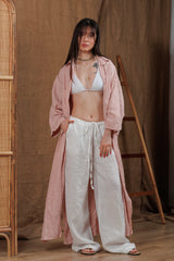 Elegant long muslin women's shirt in a soft tea rose color, styled with white linen trousers, perfect for beachwear or casual summer days. The loose fit and breathable fabric offer comfort and elegance in warm climates, ideal for the UAE and GCC market