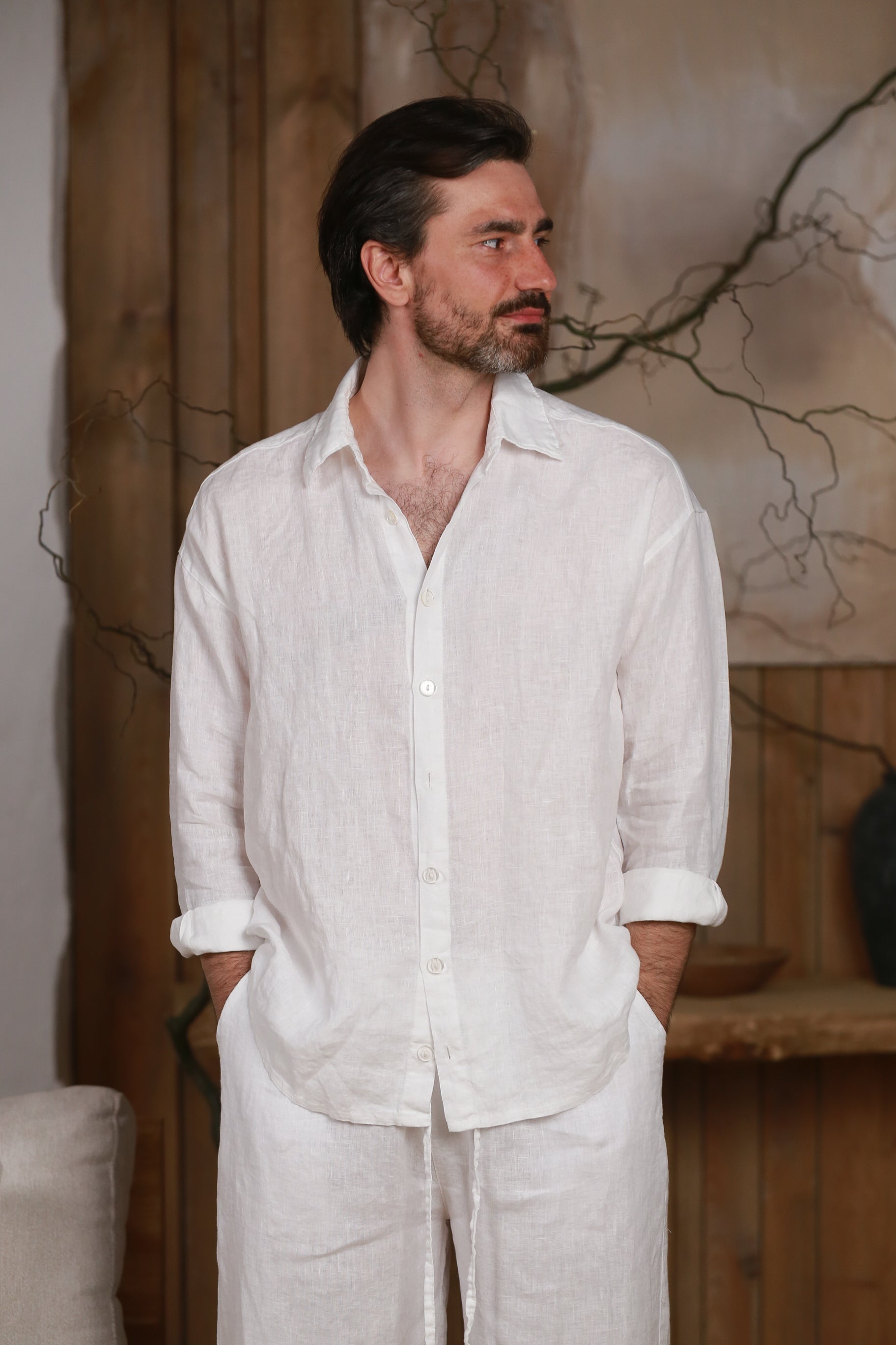 White linen men's shirt designed for the hot climate of the UAE and GCC countries. Breathable and lightweight, perfect for beach, city, and home wear. Styled in a minimalist, nature-inspired interior with wooden elements, reflecting Middle Eastern elegance and sustainable fashion.