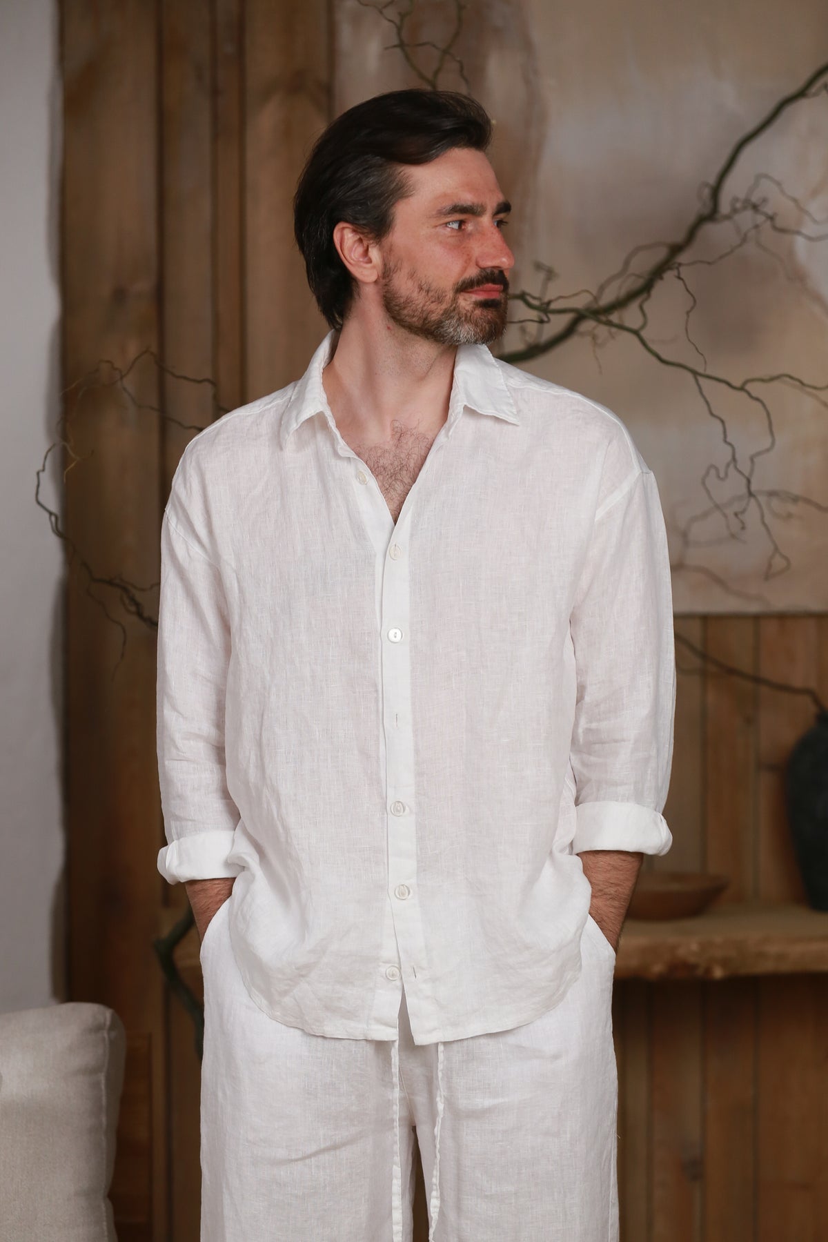 White linen men's shirt designed for the hot climate of the UAE and GCC countries. Breathable and lightweight, perfect for beach, city, and home wear. Styled in a minimalist, nature-inspired interior with wooden elements, reflecting Middle Eastern elegance and sustainable fashion.