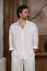 White linen men's shirt designed for the hot climate of the UAE and GCC countries. Breathable and lightweight, perfect for beach, city, and home wear. Styled in a minimalist, nature-inspired interior with wooden elements, reflecting Middle Eastern elegance and sustainable fashion.