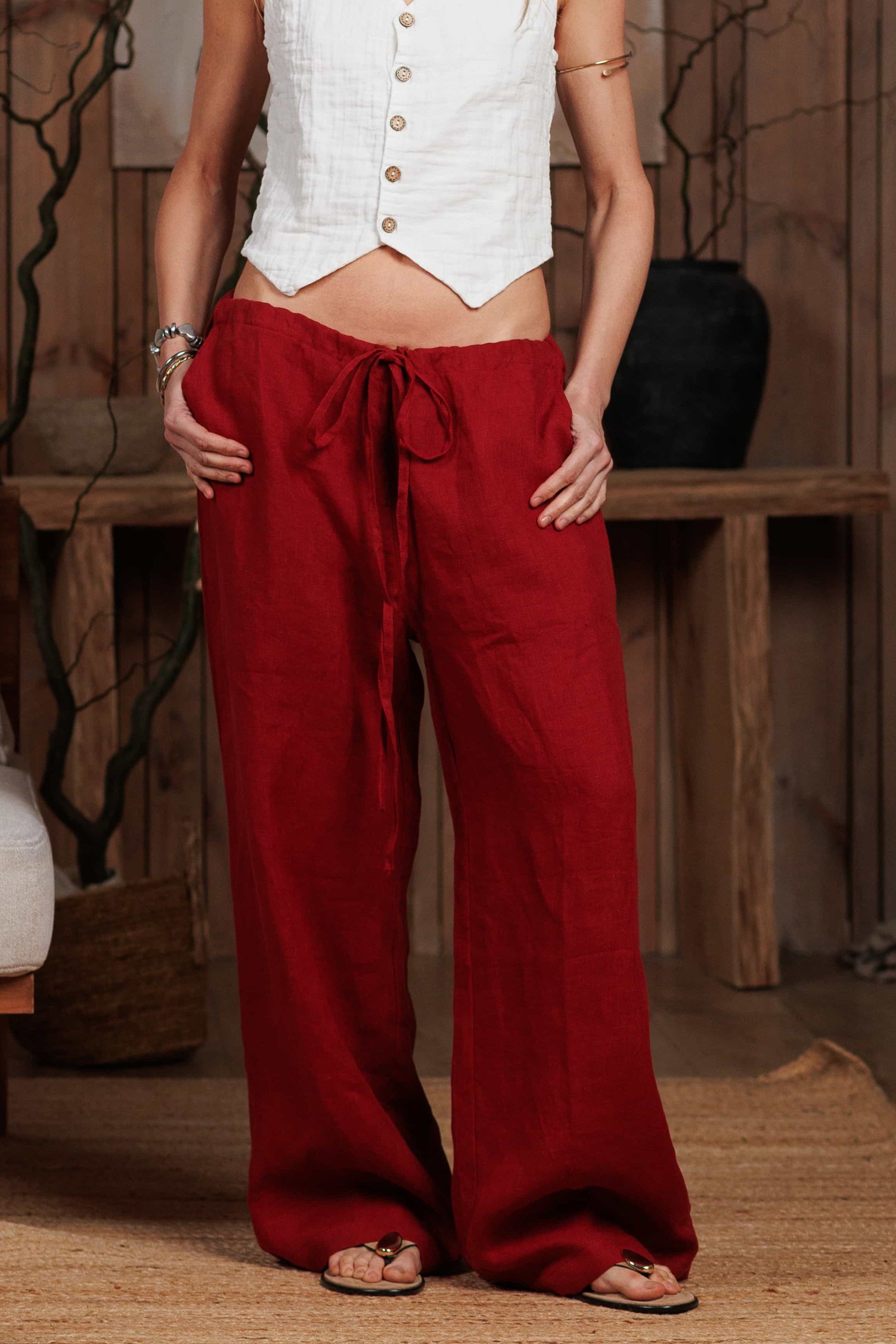 Women's burgundy red linen trousers styled with a white sleeveless buttoned top, perfect for summer and casual city looks. Lightweight, breathable, and crafted from 100% linen, ideal for hot climates in the UAE and GCC. Linen pants, summer fashion, breathable fabric, UAE style.