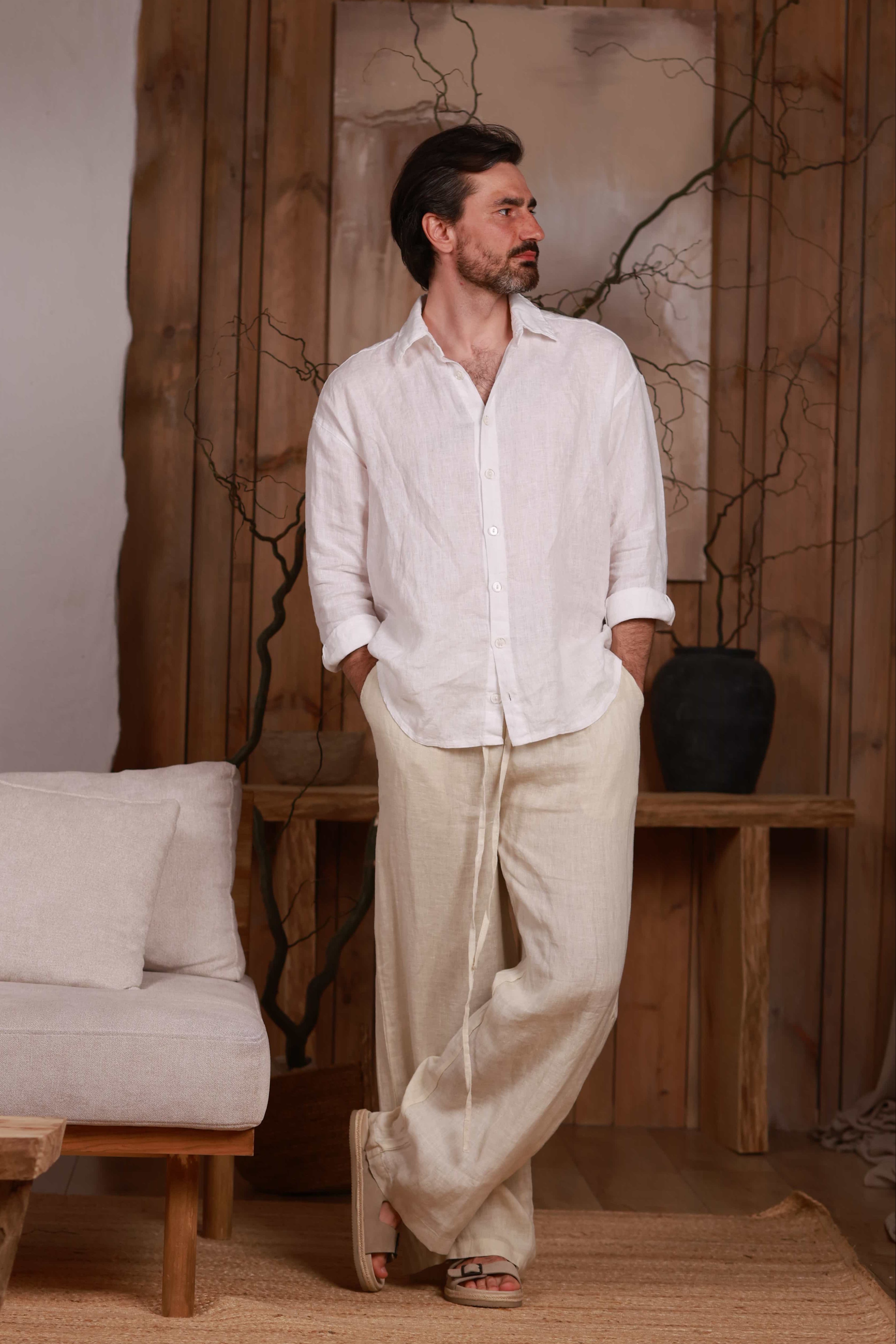 men's white linen shirt paired with beige linen trousers, highlighting the relaxed fit and natural drape of the fabric. Perfect for beach outings, city walks, and home comfort in Dubai, UAE, and GCC. Photographed in a minimalist interior, showcasing Middle Eastern elegance and sustainable fashion.