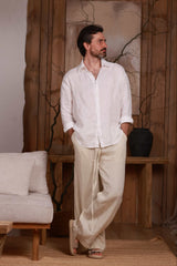 men's white linen shirt paired with beige linen trousers, highlighting the relaxed fit and natural drape of the fabric. Perfect for beach outings, city walks, and home comfort in Dubai, UAE, and GCC. Photographed in a minimalist interior, showcasing Middle Eastern elegance and sustainable fashion.